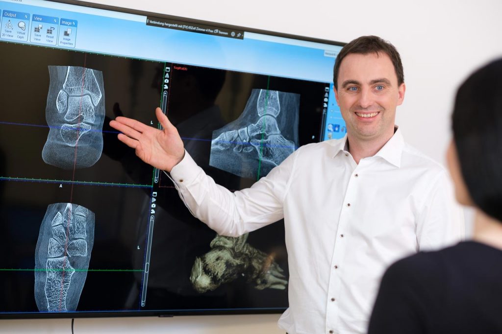 Dr. Stefan Böhr erläutert an einem großen Monitor die Röntgenbilder des Patienten
